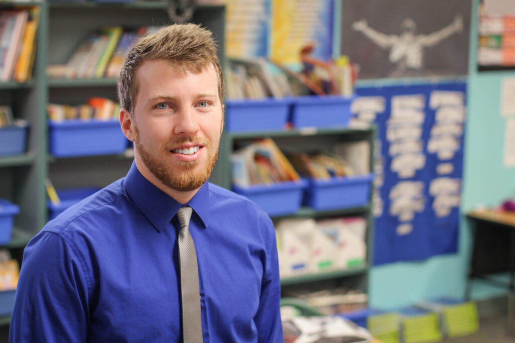 Teacher smiling at camera while in his decorated classroom.