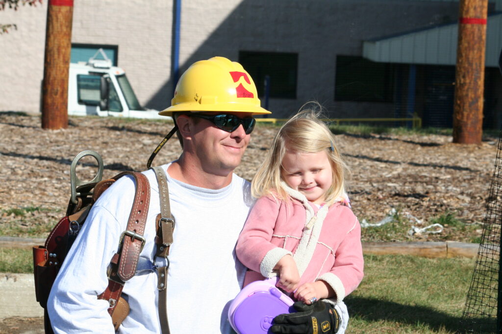 Man in helmet carrying a little girl, both smiling at the camera.