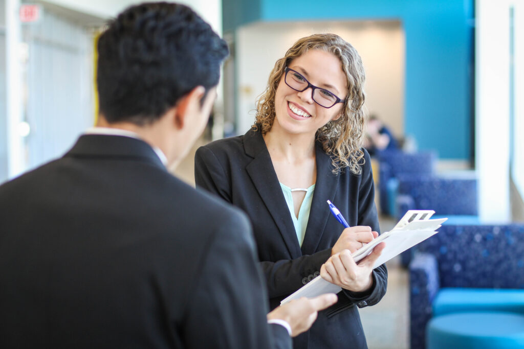 Business woman with clipboard smiling at business man