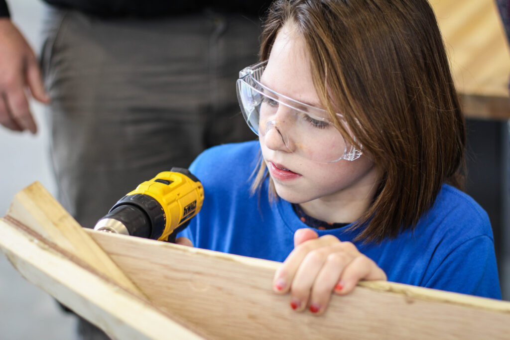 Girl drilling into a wooden board.