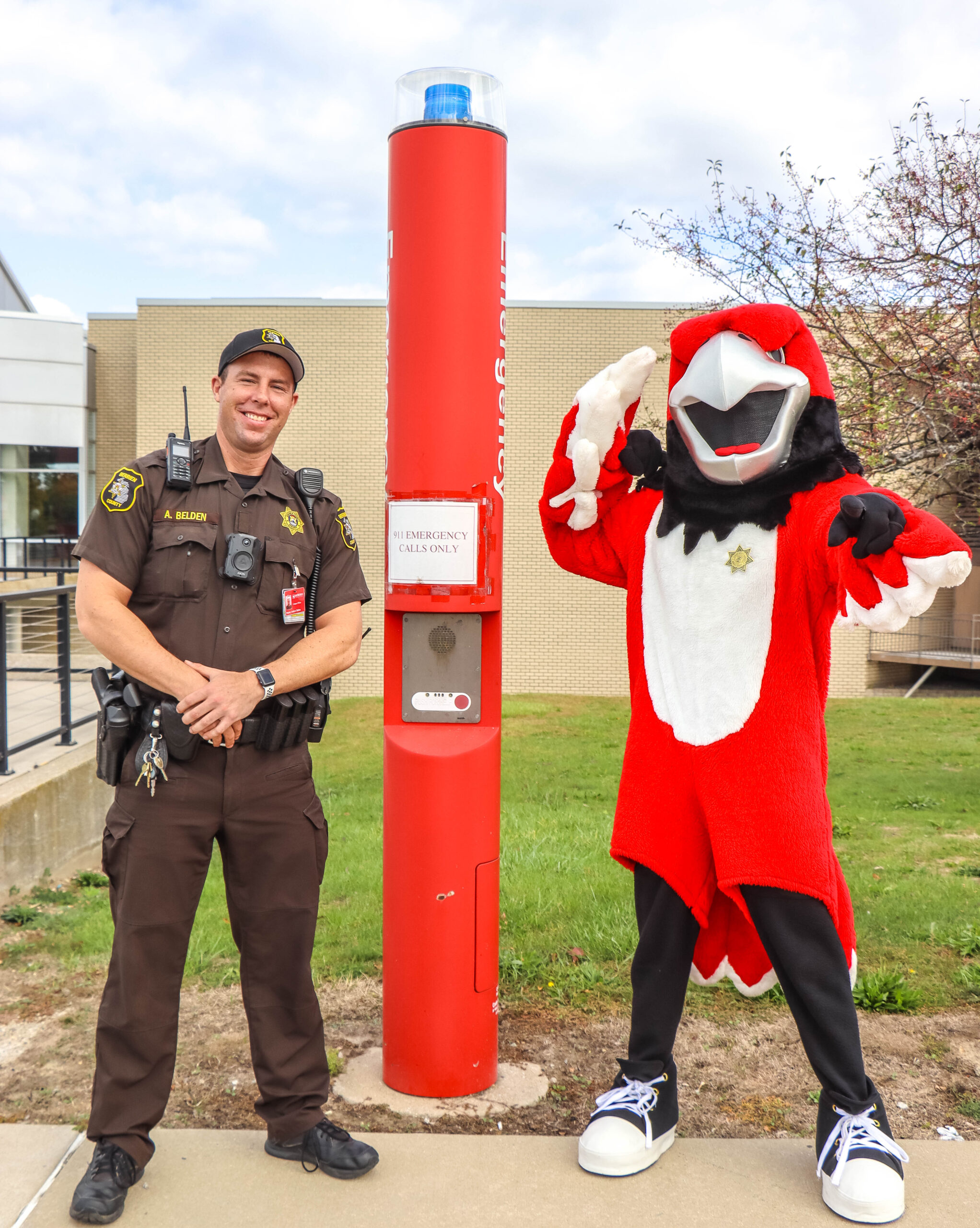Security man and LMC mascot standing proudly next to emergency call station.