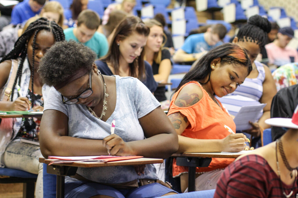 Many students writing at their desks in a large classroom